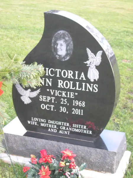 A polished black granite monument with a curved profile, an etched portrait, a carved angel and dove, the full name and a relationship line