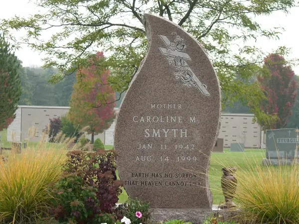 A rose granite monument cut as a rising flame or leaf, with a carved angel at the top, a relationship line above the name and an epitaph below