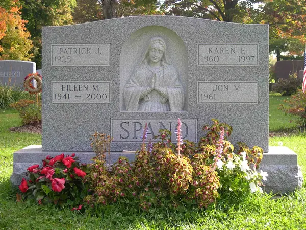 A grey granite monument with a carved figure of the Virgin Mary at its centre, four name tablets around it and the family name on a raised panel at the foot