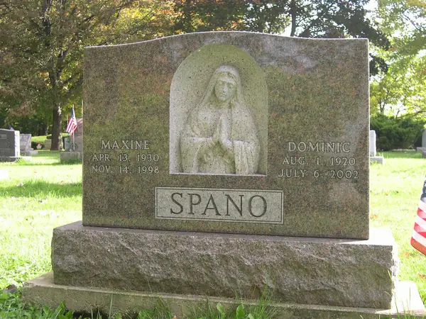 A grey granite monument with a deeply carved Madonna figure in a niche, two names either side and the family name on a raised panel