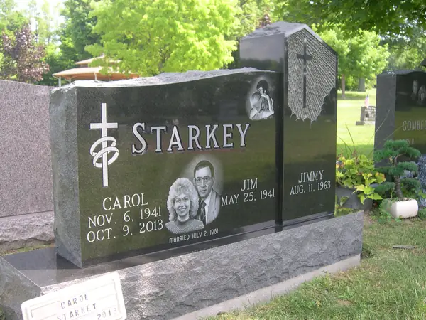 A polished black granite monument in two sections, the taller carrying etched portraits and a cross, the shorter a single name beneath a carved shroud and cross