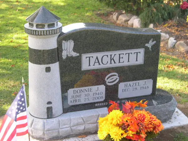 A dark granite monument paired with a freestanding granite lighthouse, with a carved hummingbird, two name tablets and a marriage emblem