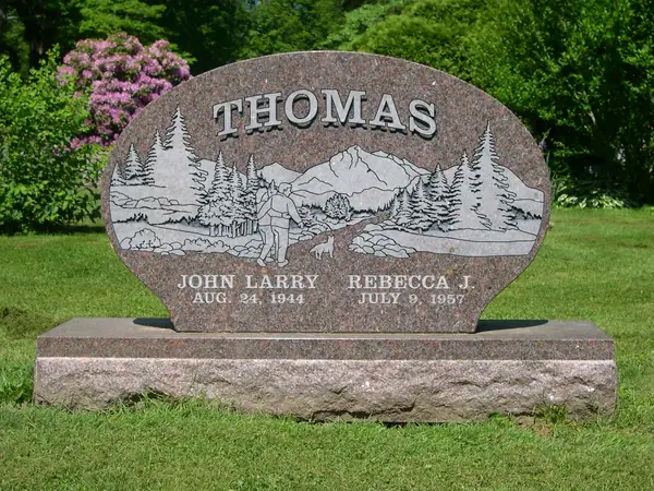 A rose granite monument with a rounded top, an etched scene of a man walking a dog among pines and mountains, and two name tablets below