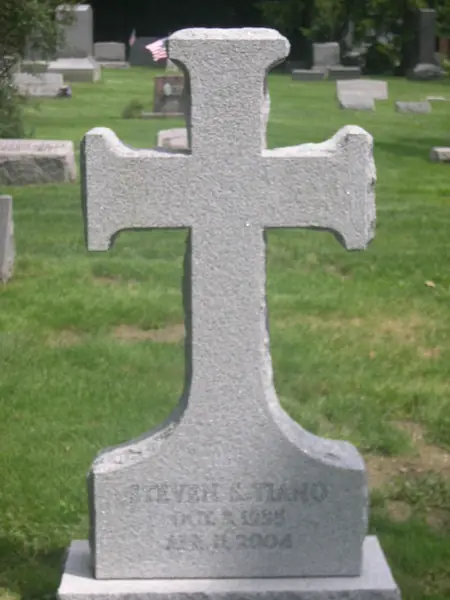 A light grey granite monument cut in the shape of a Latin cross, carrying a single name and dates