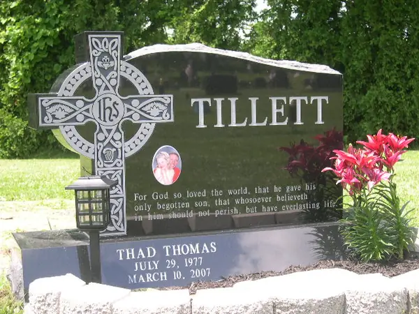A polished black granite monument with an ornate Celtic cross carved at one side, the family name in raised lettering, a small oval portrait and a scripture verse