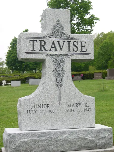 A light grey granite cross-shaped monument with a carved floral vine down its centre, the family name across the arms and two names below