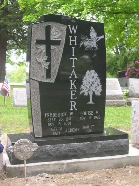 A polished black granite monument with an asymmetric profile, a carved cross with lilies, an etched cardinal and tree, and the family name set vertically
