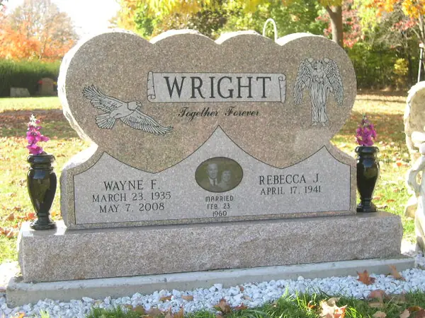A rose granite monument with a scalloped top, a carved eagle at one side and an angel at the other, an oval etched portrait and a marriage date