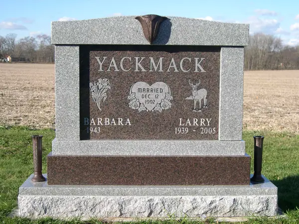 A two-tone monument with a grey granite frame and dark red panel, carved florals and a deer, a heart-shaped marriage plaque and two names