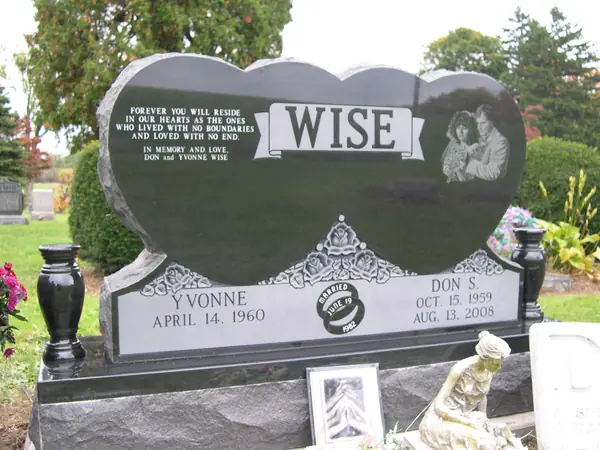 A polished black granite monument cut as two joined hearts, with an etched couple's portrait, a long epitaph, a carved crown and a marriage emblem