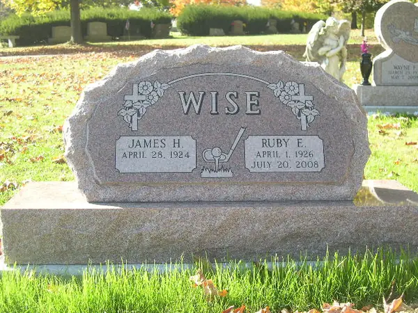 A grey granite monument with a rounded top, carved crosses and roses at both corners, a raised name panel and a small carved emblem between two names