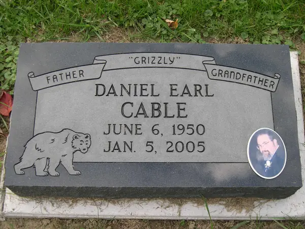 A polished dark granite marker with relationship lines on a carved banner, an etched bear, an oval portrait and a nickname in quotation marks