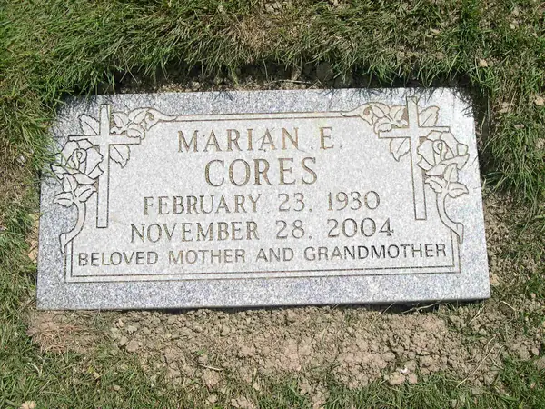 A grey granite bevel marker carved with roses and crosses at both sides, carrying a full name, dates and a relationship line