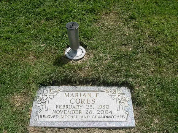 A small flush granite marker set level with the lawn beside a metal flower holder, carved with roses and crosses and a relationship line