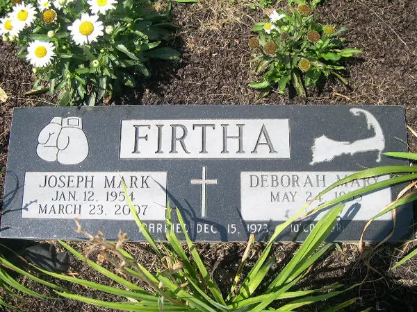 A polished dark granite bevel marker with etched boxing gloves at one side and a fish at the other, a cross between two names and a marriage date