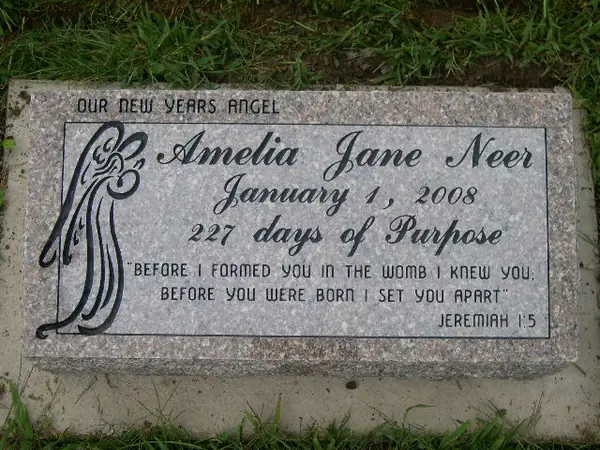 A light grey granite marker with a carved art-nouveau border, an infant's name in script and a scripture verse