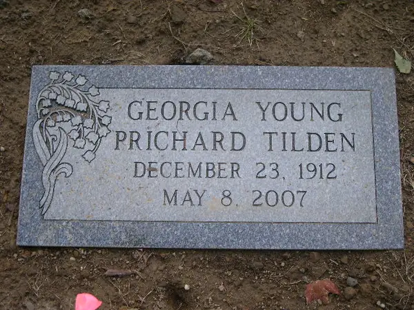A grey granite flat marker with a carved floral spray at one corner, carrying a full name and dates in cut lettering