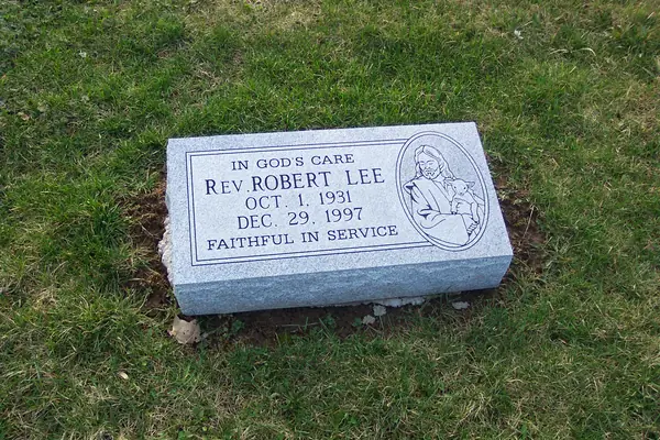 A light grey granite bevel marker with an etched oval of Christ the Good Shepherd, a name and dates, and a short epitaph above and below
