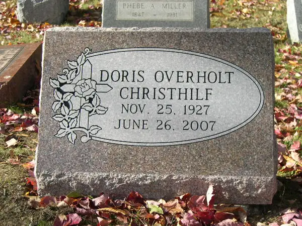 A rose granite slant marker with an oval border carved with a cross and roses, carrying a full name, a maiden name and dates