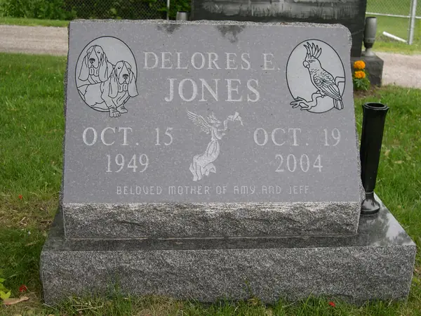 A grey granite slant marker with etched ovals of two dogs and a cockatoo, a carved cherub between the dates and a relationship line across the foot