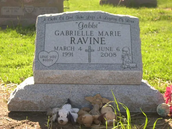 A rose granite slant marker with a cross between two dates, a heart at one corner and a carved figure of a child at the other, with a nickname in quotation marks