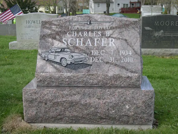 A rose granite slant marker with an etched classic car, a relationship line above the name and dates alongside