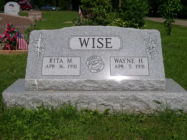 A light grey granite slant marker with crosses and roses carved at both corners, two name tablets and a marriage emblem between them
