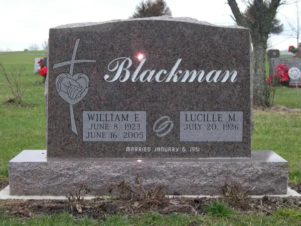 A rose granite upright monument with the family name in script, a cross and clasped hands carved beside it, and a marriage date cut below the name tablets
