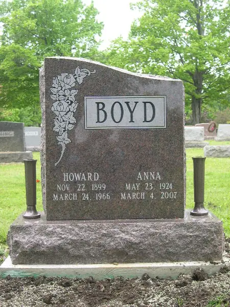 A rose granite upright monument with a wave-shaped top, a raised name panel and morning glories carved down one side, with bronze vases either side