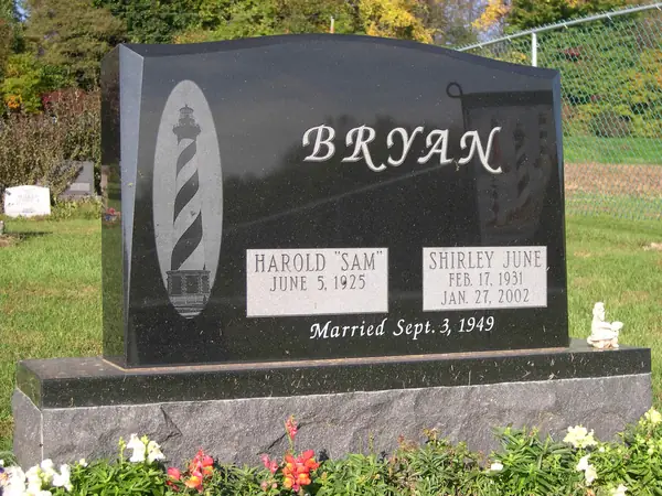 A polished black granite slant-faced monument with an etched lighthouse, the family name in script and a marriage date beneath the name tablets