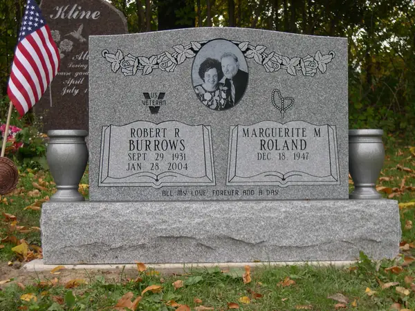 A light grey granite upright monument with an etched oval portrait framed by carved roses, a veterans emblem, two raised name tablets and an epitaph across the foot