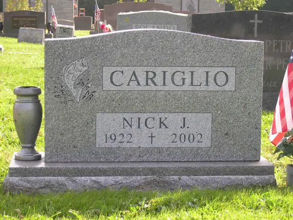 A grey granite upright monument with a leaping fish carved at one shoulder, a raised name panel and a single name tablet, with a matching granite vase alongside