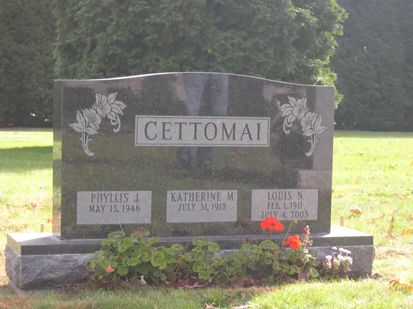 A dark granite upright monument with a serpentine top, flowers carved at both shoulders and three name tablets across the face