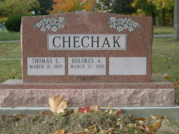 A rose granite upright monument with carved flowers at the upper corners, a raised name panel and three name tablets, one left blank for a later inscription