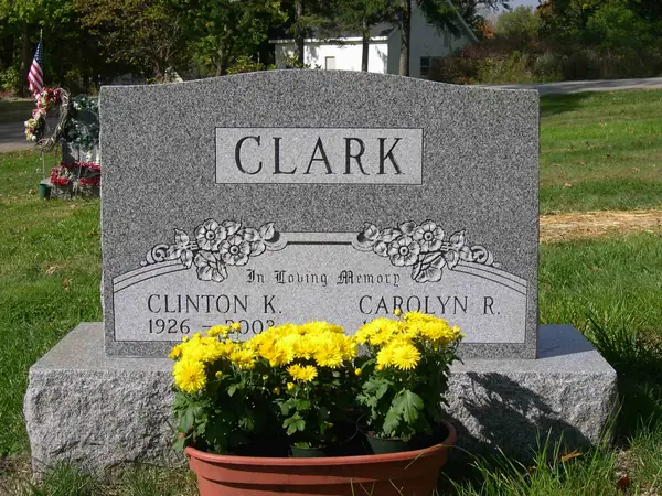A light grey granite upright monument with a shaped top, a raised name panel and a carved floral swag above two name tablets