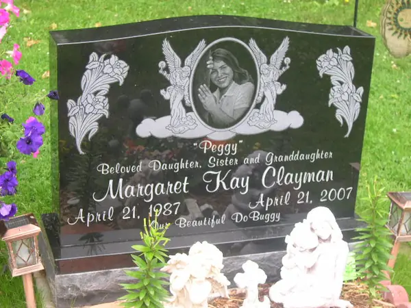 A polished black granite upright monument with an etched oval portrait set among carved lilies and clouds, the name in script and an epitaph below