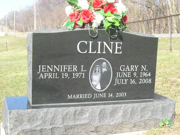 A polished black granite upright monument with an etched oval wedding portrait between two name tablets and a marriage date cut below, on a rock-pitched base