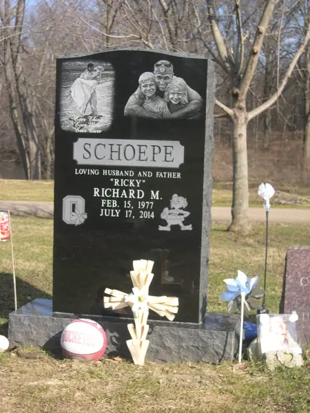 A polished black granite upright monument with an etched family group portrait and a fishing scene above a raised name panel
