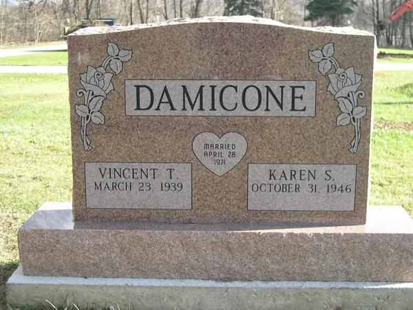 A rose granite upright monument with roses carved at both shoulders, a raised name panel and a heart-shaped marriage plaque between two name tablets