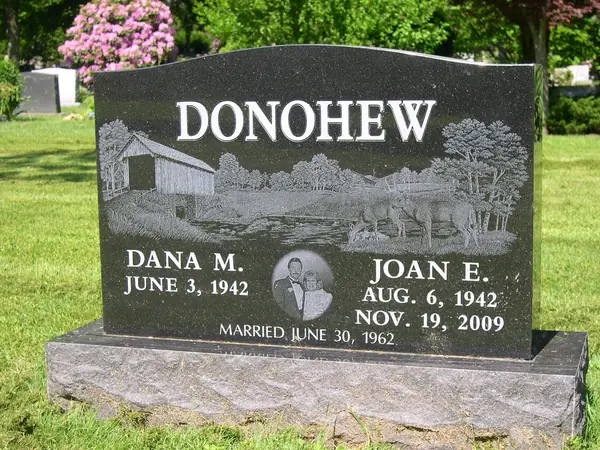 A polished black granite upright monument with a wide etched scene of a covered bridge and grazing horses, and a small etched portrait between the name tablets