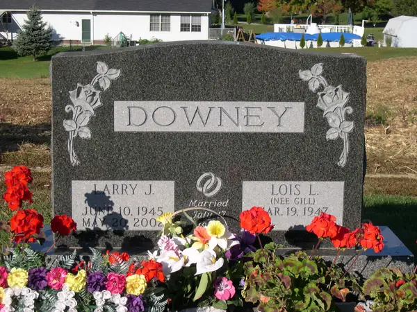 A grey granite upright monument with a raised name panel, roses and leaves carved at both shoulders and a marriage emblem between the name tablets