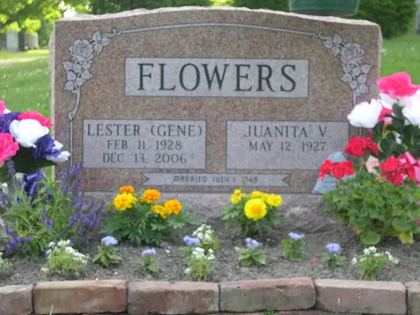 A rose granite upright monument with a raised name panel, roses carved at both upper corners, two name tablets and a marriage date across the foot