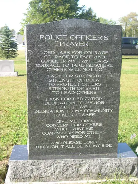 A dark grey granite upright monument cut with the full text of a police officer's prayer, on a rock-pitched base