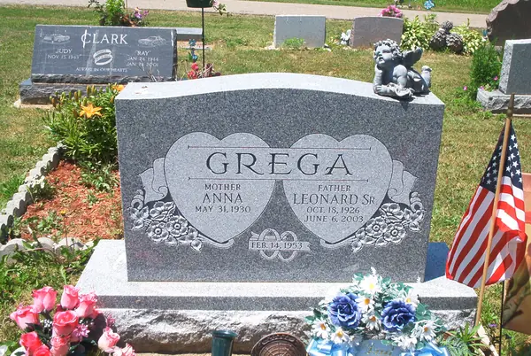 A grey granite upright monument with two interlocking hearts carved around the names, a floral scroll below and a marriage date on a banner