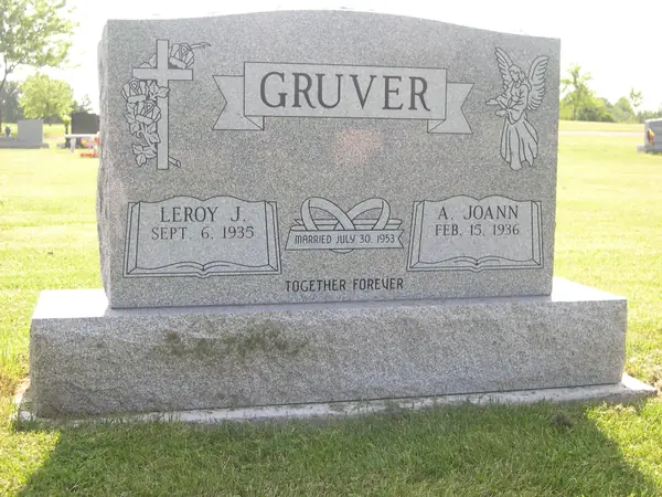 A light grey granite upright monument with a carved cross and rose at one shoulder and an angel at the other, an open book between the name tablets and an epitaph below