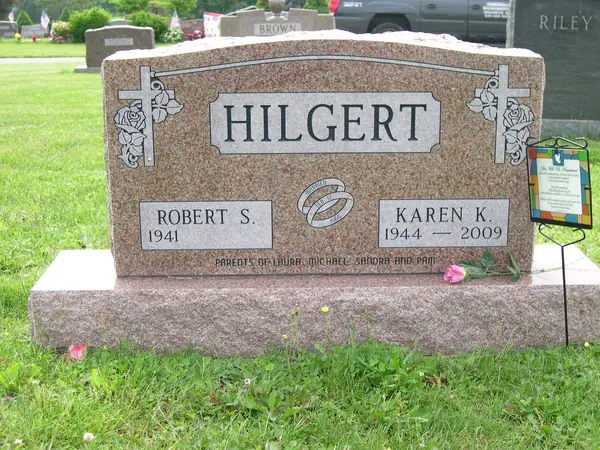 A rose granite upright monument with carved crosses and roses at both shoulders, a raised name panel and a wedding-ring emblem between the name tablets
