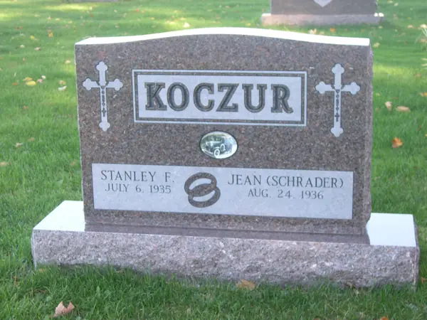 A rose granite upright monument with a raised name panel, carved crosses at both shoulders and a wedding-ring emblem between the two name tablets