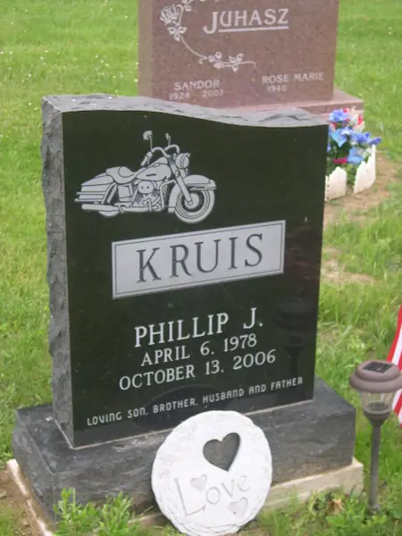 A polished black granite upright monument with an etched touring motorcycle above a raised name panel and a relationship line across the foot