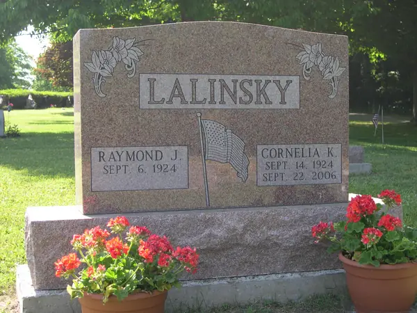 A rose granite upright monument with carved flowers at both upper corners, a raised name panel and an etched American flag between the two name tablets
