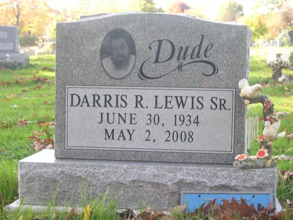A grey granite upright monument with an etched oval portrait, a nickname in large script and the full name and dates in raised lettering below